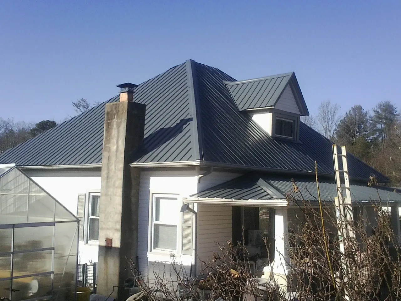 Dark blue standing seam metal roof on a white farmhouse with dormer — Slate & Tile Roof Repair by Roofing Brothers in Freeman